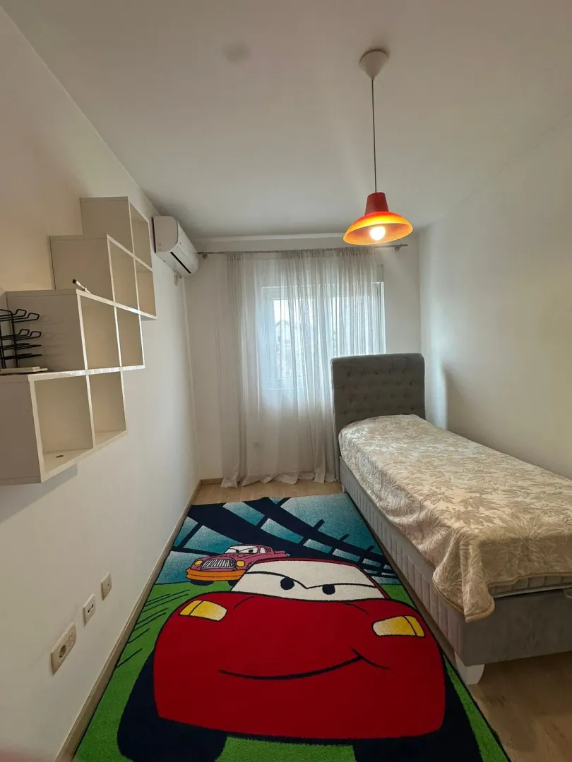 Dječija soba sa krevetom za jednu osobu, zidnim policama i šarenim tepihom.