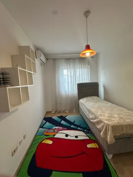 Dječija soba sa krevetom za jednu osobu, zidnim policama i šarenim tepihom. - image 5
