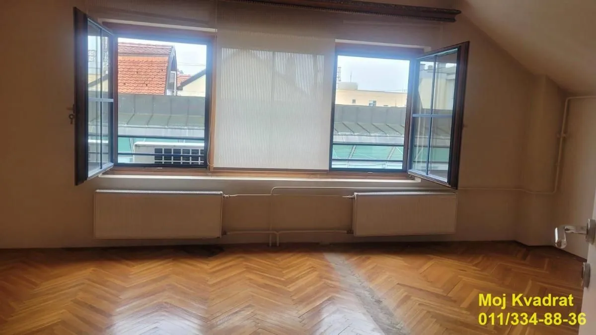 Empty room with parquet flooring and open windows.