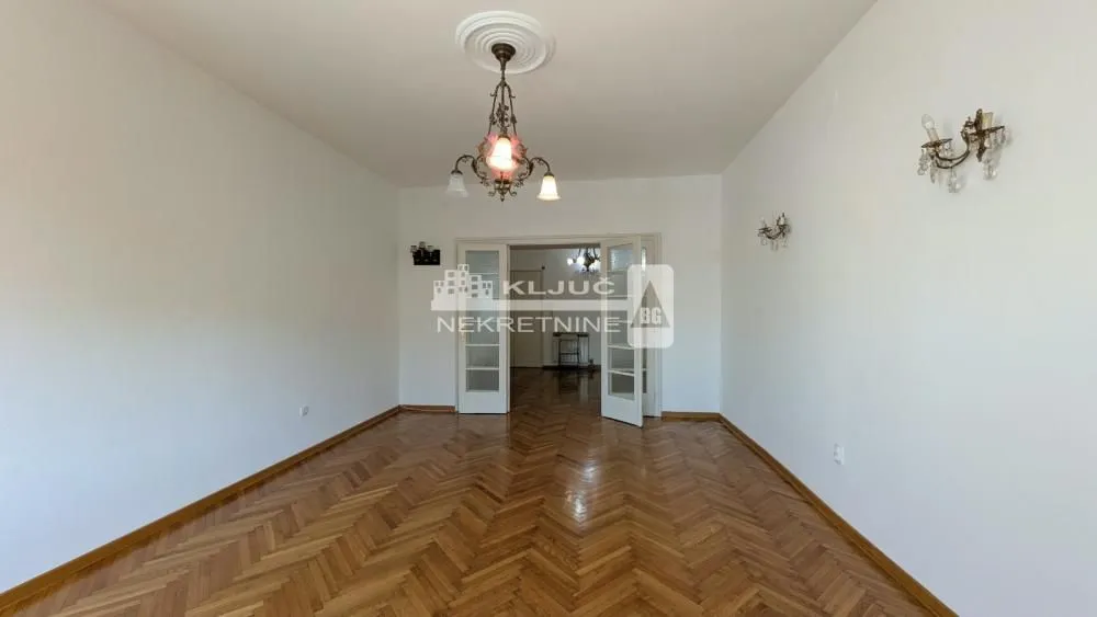 Empty room with wooden parquet flooring and double doors.