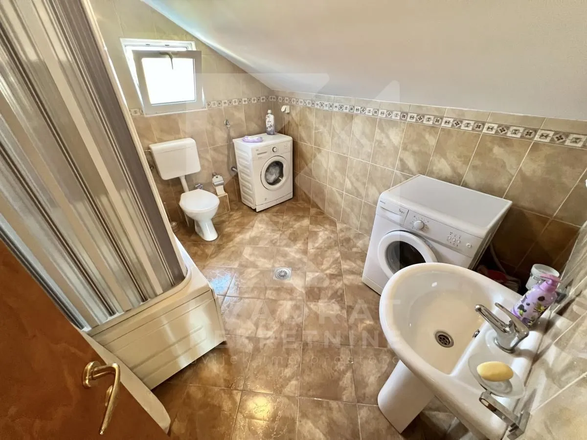 Bathroom with tiles, bathtub, toilet, washbasin, and two washing machines.