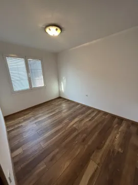 Prazna soba sa bijelim zidovima, tamnim drvenim podom i prozorom. - image 14