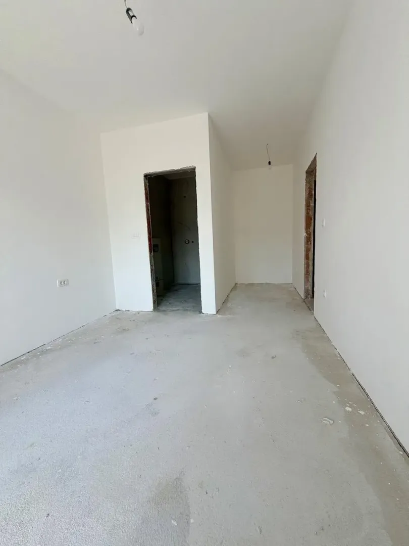 Prazna prostorija u neopremljenom stanu u fazi izgradnje sa bijelim zidovima i betonskim podom.