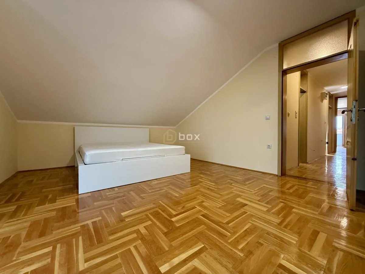 Empty bedroom with a double bed and wooden parquet flooring.