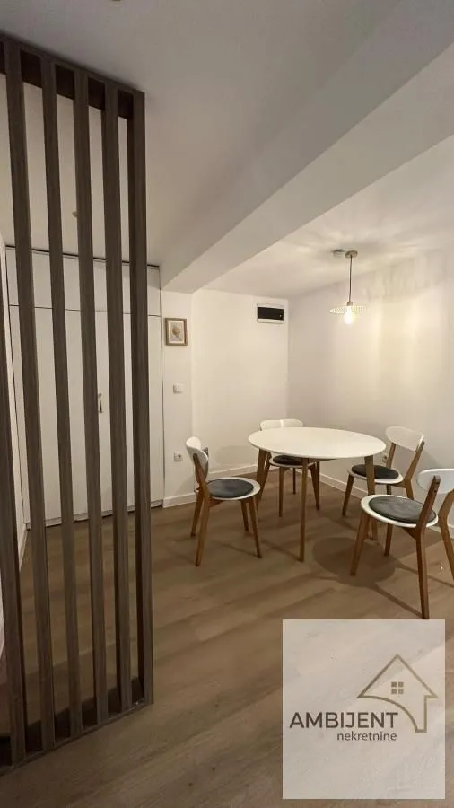 Dining area with a round table and white chairs separated by a wooden partition panel.