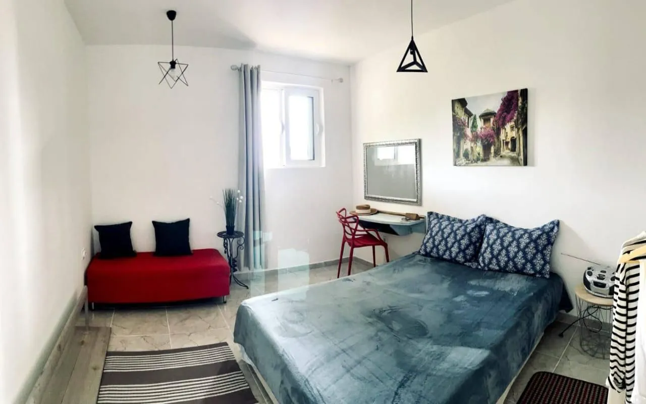 Furnished bedroom with a double bed, red sofa, and a desk.