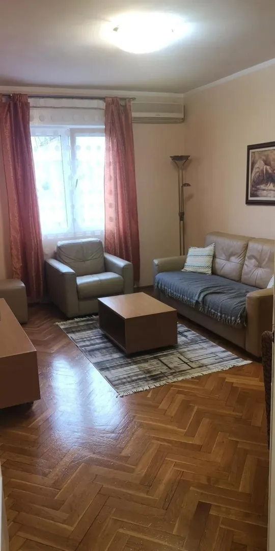 Dnevna soba sa kožnom garniturom, drvenim klub stolom i parketom.