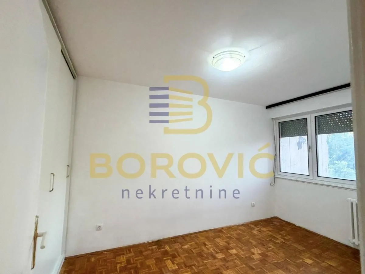 Prazna soba sa prozorom i drvenim parketom.