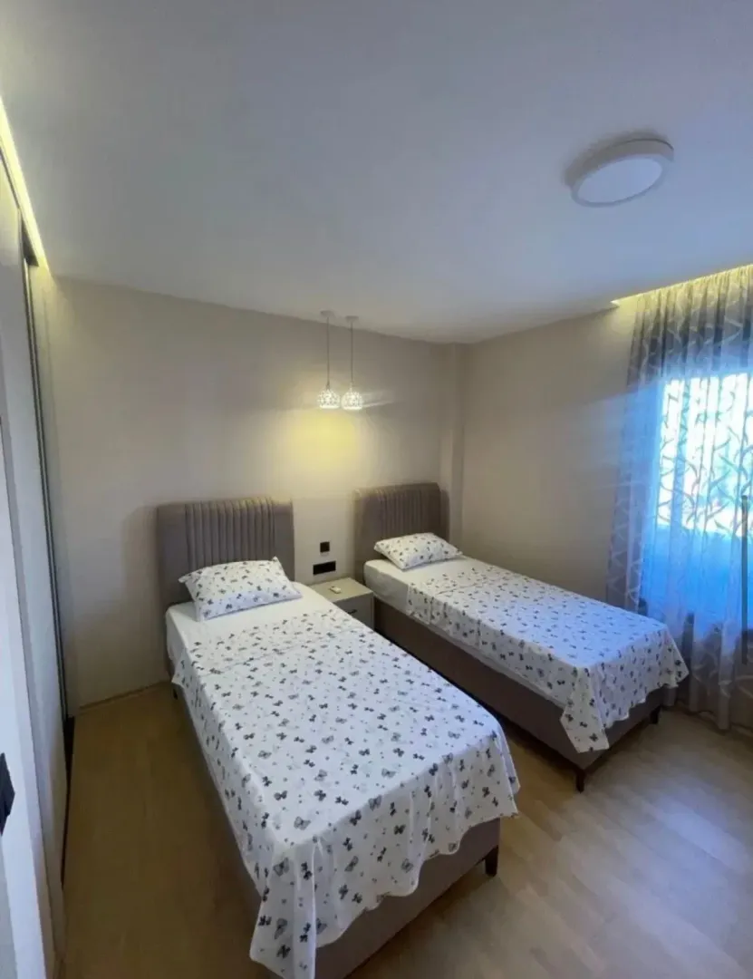 Spavaća soba sa dva singl kreveta, noćnim stočićem i prozorom sa zavjesama.