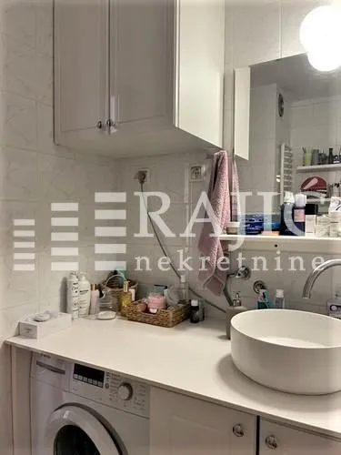 Small bathroom with a basin, washing machine, and white cabinets.