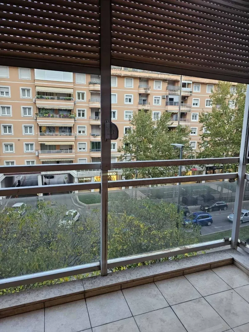 Pogled sa balkona na susjednu zgradu i ulicu sa drvećem.