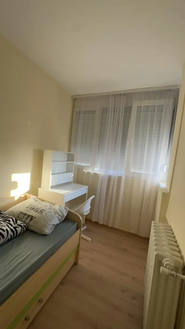 Manja spavaća soba sa krevetom, radnim stolom i prozorom.