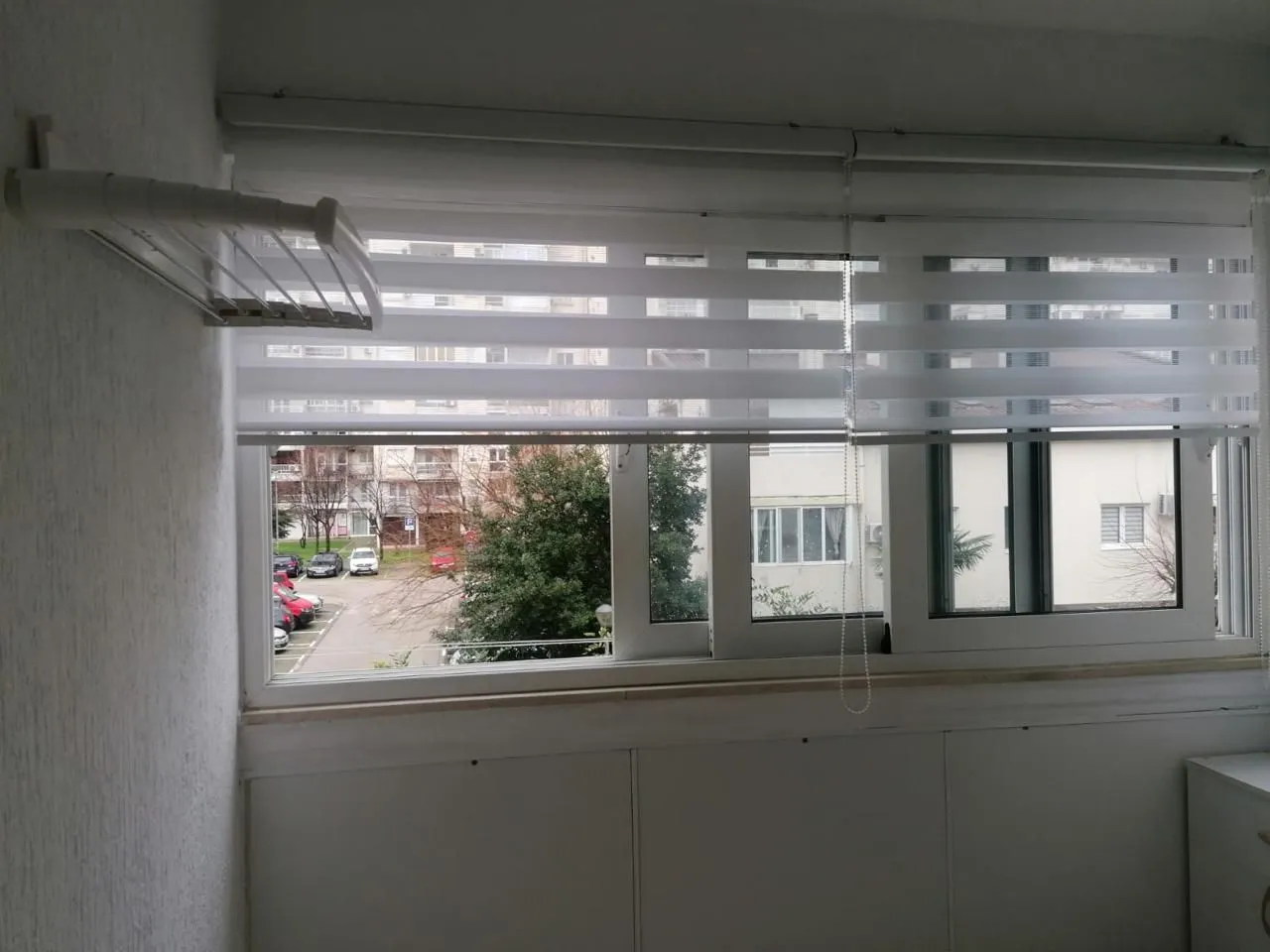Enclosed balcony with blinds and a view of the parking lot and buildings.