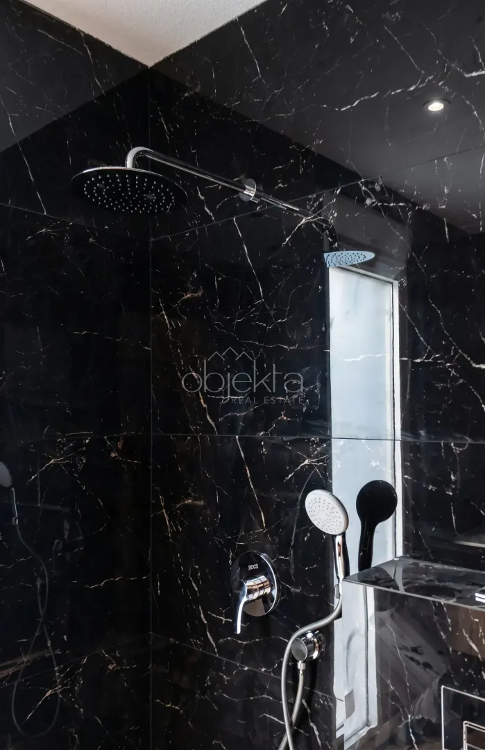 Shower enclosure with dark marble tiles and a modern faucet.