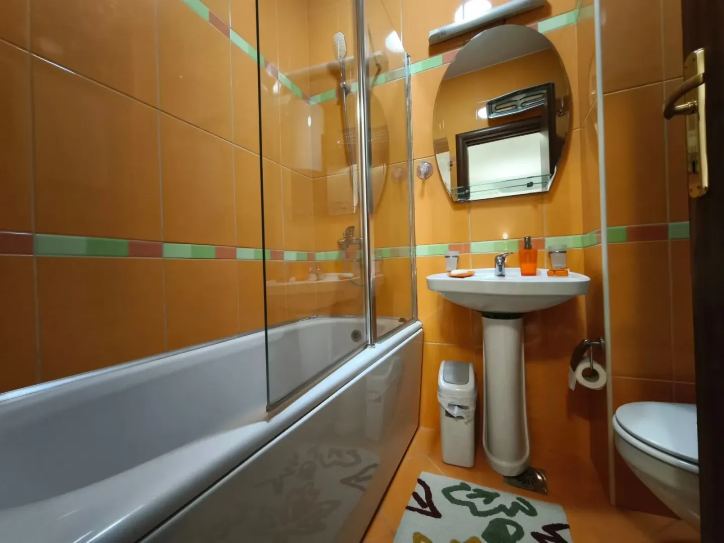 Kupatilo obloženo narandžastim pločicama sa kadom, umivaonikom i WC šoljom.