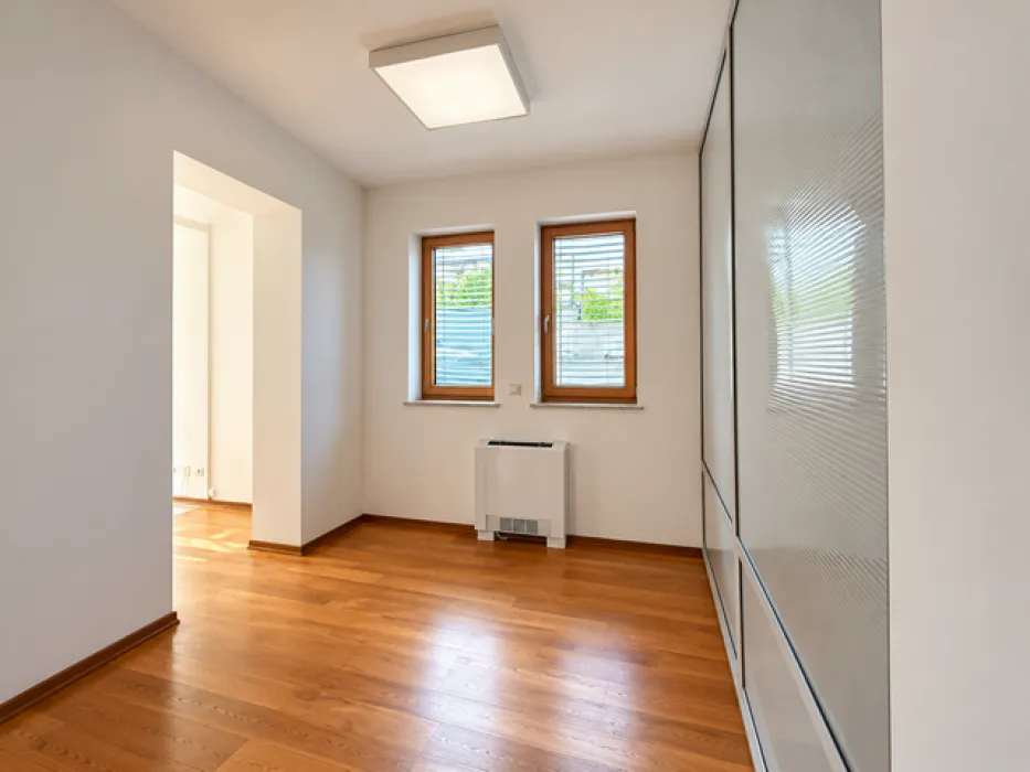 Empty room with wooden flooring, two windows, and a built-in wardrobe.