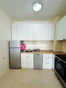Prikaz manje kuhinje sa bijelim elementima, frižiderom i šporetom. - image 6