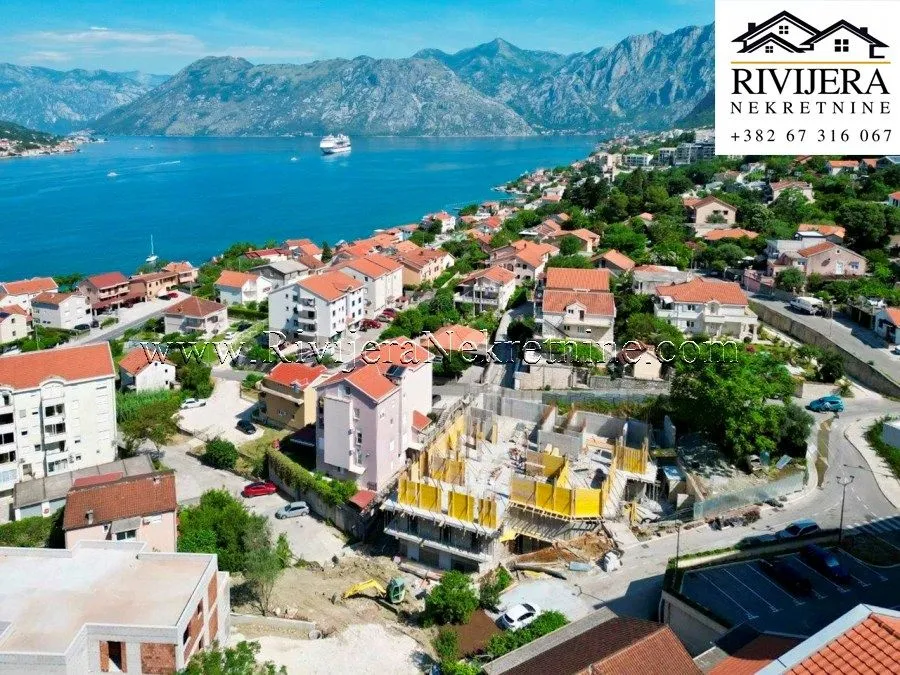 Pogled iz vazduha na gradilište i naselje pored mora sa planinama u pozadini.