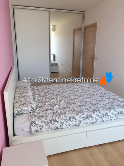 Nameštena spavaća soba sa bračnim krevetom i velikim ugradnim garderoberom sa ogledalom.