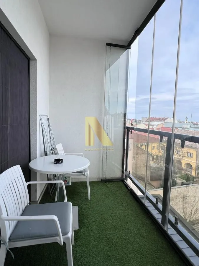 Zastakljeni balkon sa stočićem, stolicama i veštačkom travom na podu.