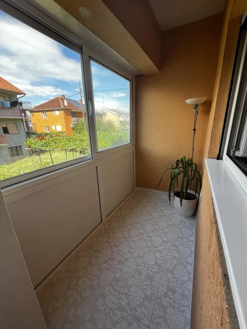 Zatvoreni balkon sa pločicama i pogledom na okolinu.