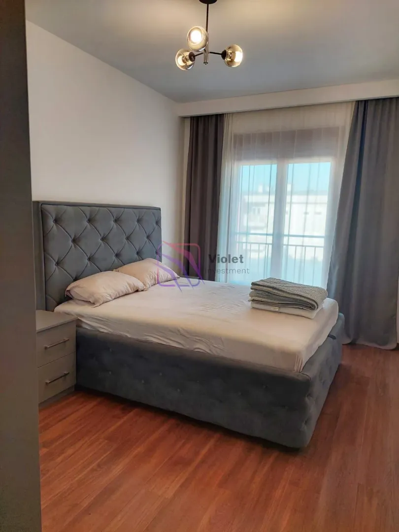 A bedroom featuring a double bed, a nightstand, and a window with curtains.