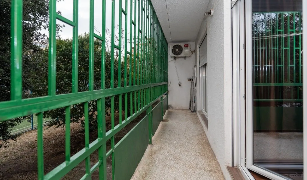 Long balcony with a green railing and an outdoor air conditioning unit.
