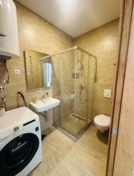 Small bathroom with a shower cabin, sink, toilet, and washing machine. - image 4