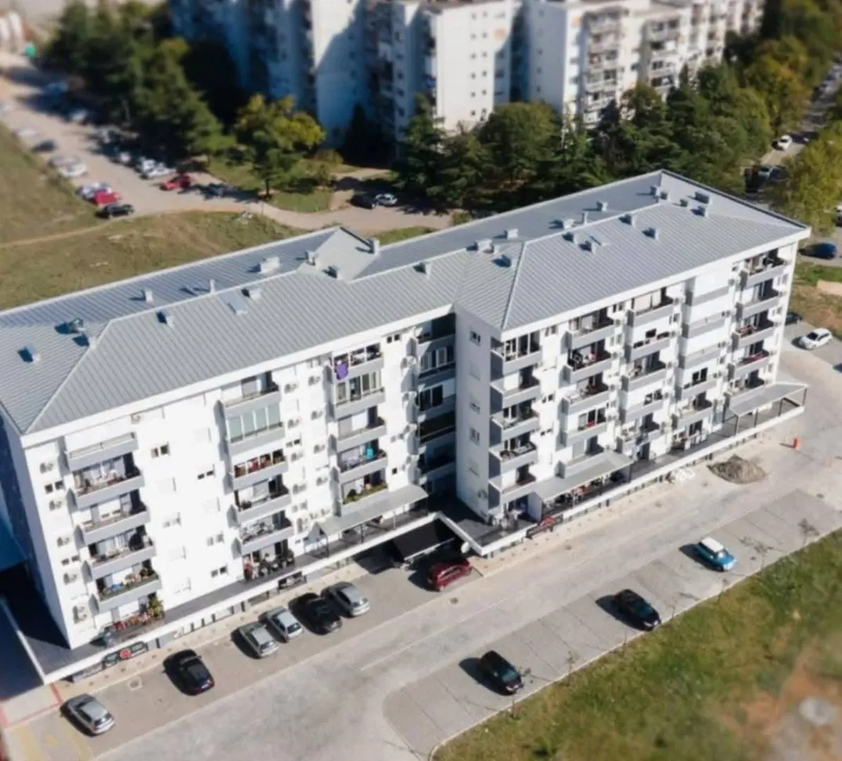 Pogled iz vazduha na stambenu zgradu i parking sa okolnim zelenilom.
