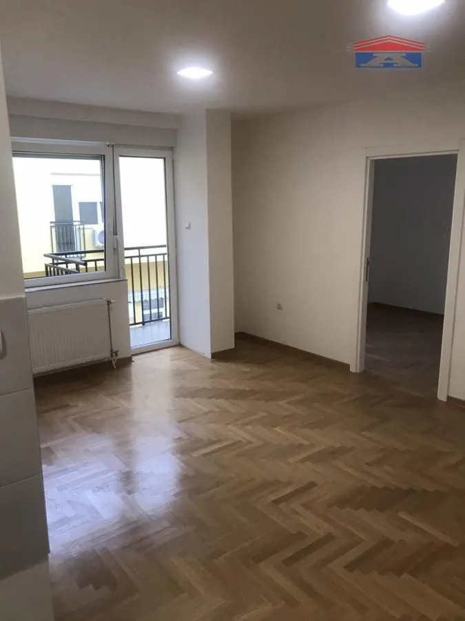Empty room with parquet flooring, a window, and a door leading to the balcony.