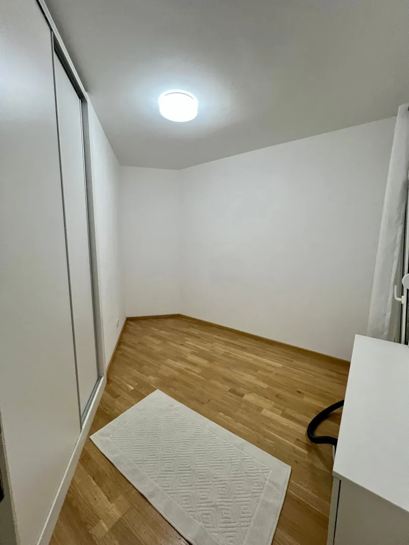 Prazna soba sa ugradnim plakarom, drvenim podom i bijelim zidovima.