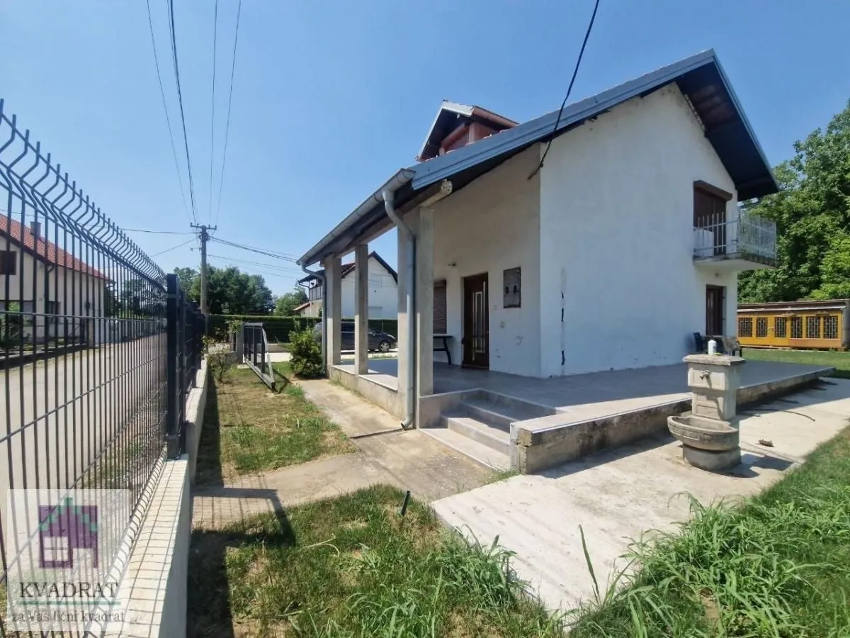 Pogled na dvorište i spoljašnjost kuće sa popločanom terasom i ogradom.