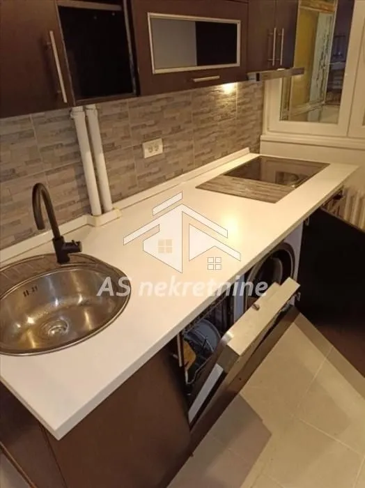 Kitchen with a white countertop, sink, built-in cooktop, and an open dishwasher.
