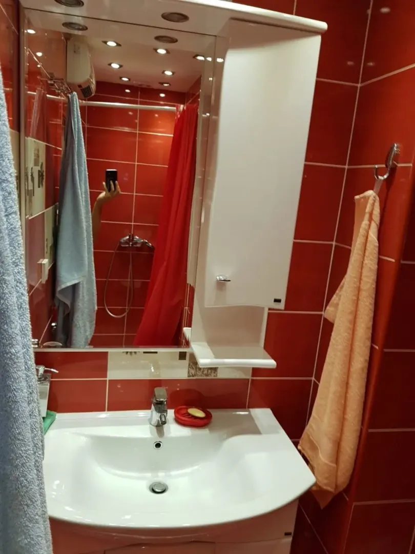 Kupatilo sa crvenim pločicama, bijelim lavaboom i ogledalom.