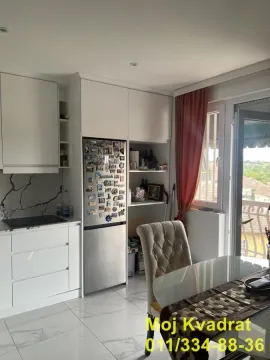 Bela kuhinja sa ugrađenim elementima i trpezarijskim stolom pored prozora. - image 4
