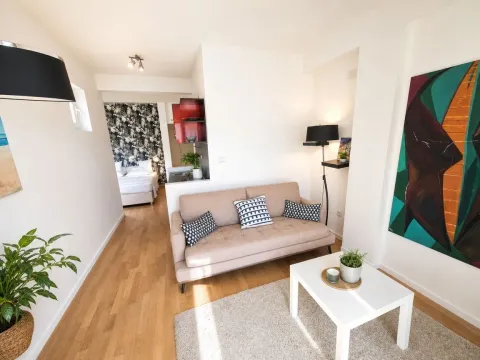 Living room with a sofa, coffee table, and a view of the bedroom in the background. - image 9