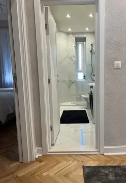 View through a doorway into a modern bathroom with a shower and washing machine. - image 16