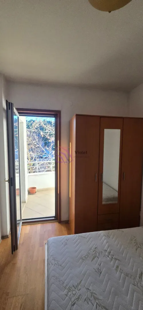 Spavaća soba sa krevetom, drvenim ormarom i izlazom na terasu.
