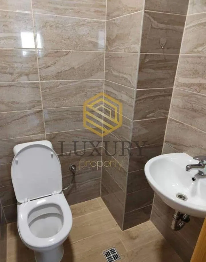 Manje kupatilo sa WC šoljom i umivaonikom, obloženo keramičkim pločicama.