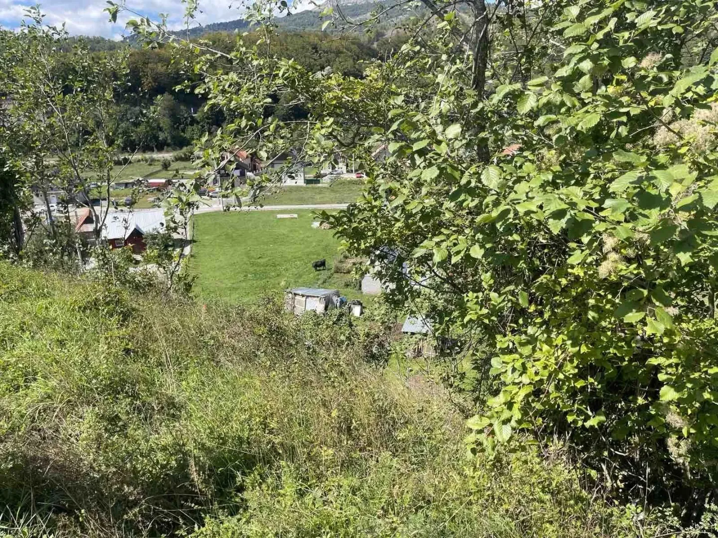 Pogled sa uzvišenja na zelenu parcelu i okolni prirodni pejzaž.