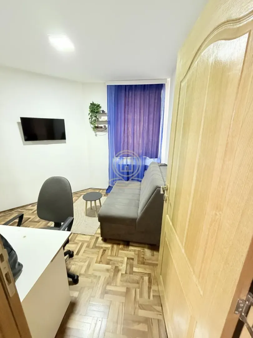 Dnevni boravak sa kaučem, radnim stolom i televizorom na zidu.