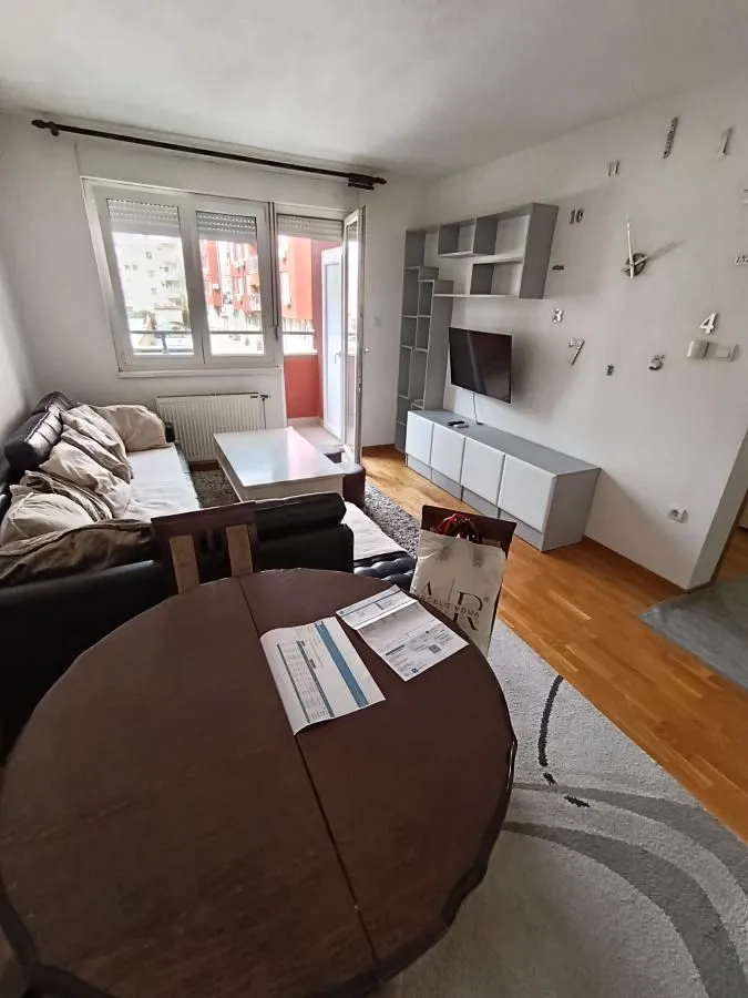 Dnevna soba sa garniturom, trpezarijskim stolom i izlazom na balkon.