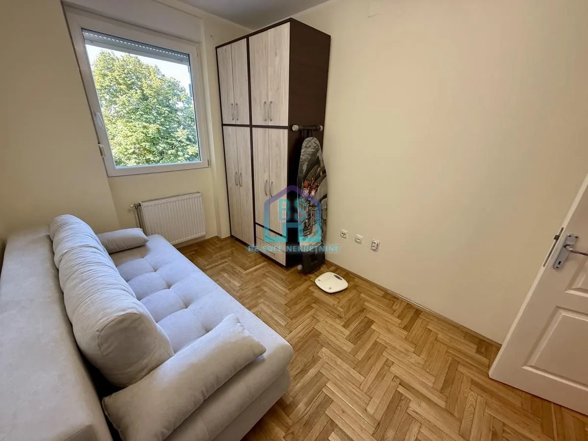 Dnevna soba sa garniturom za sedenje, ormarom i drvenim podom.