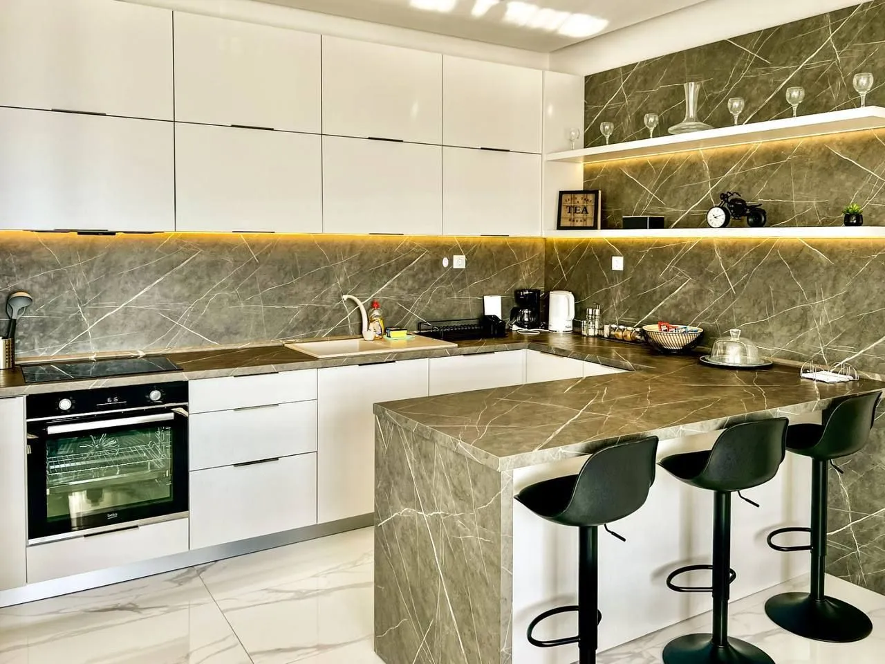 Modern kitchen with white cabinets, marble countertops, and a breakfast bar with bar stools.