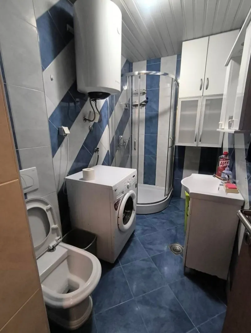 Compact bathroom with a shower cabin, washbasin, and washing machine.