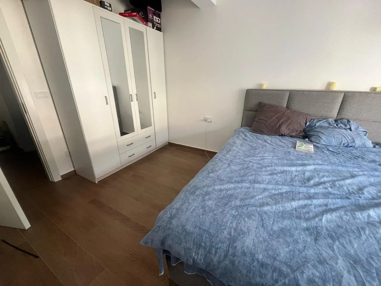 Spavaća soba sa bračnim krevetom, bijelim garderoberom i drvenim podom.
