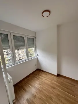 Prazna soba sa parketom i prozorom koji gleda na zgrade. - image 11