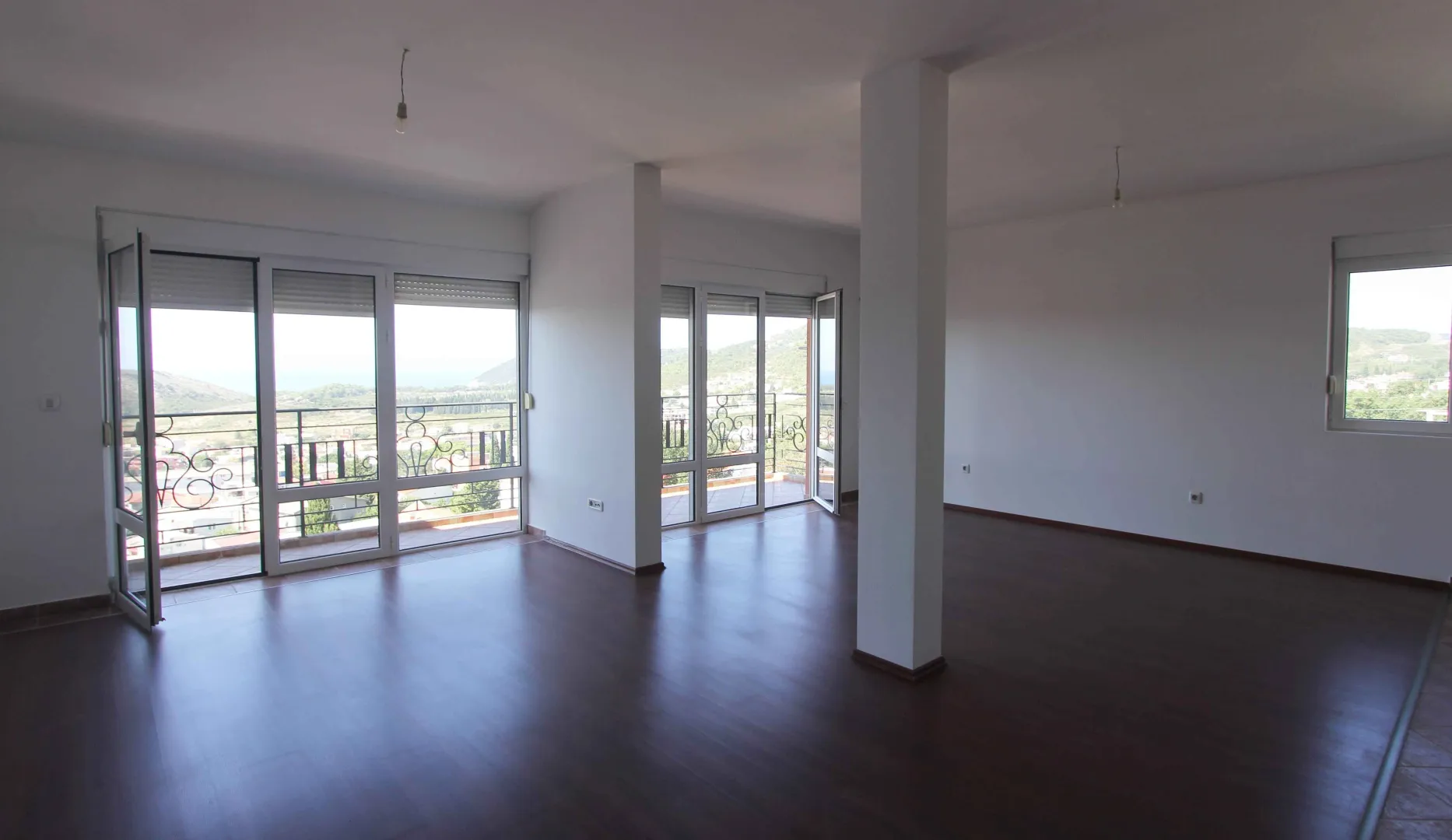 Svijetla i prostrana prazna soba sa tamnim podom i izlazom na balkon.