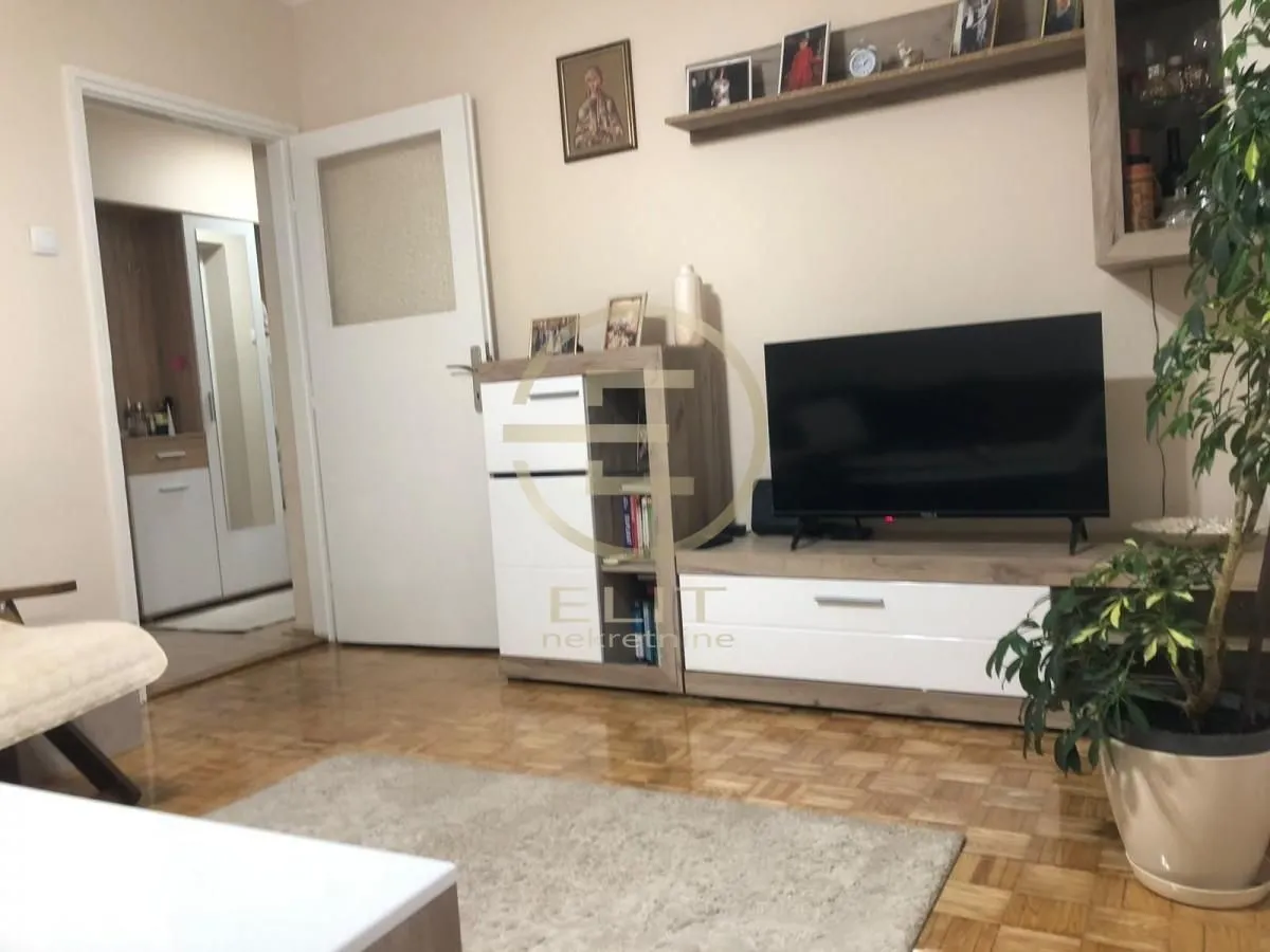 Dnevna soba sa TV komodom i parketom na podu.