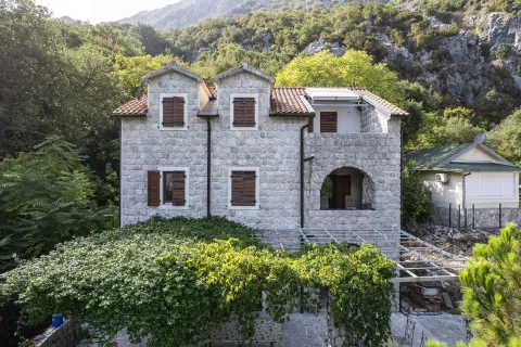 Pogled na prednju fasadu tradicionalne kamene kuće sa drvenim kapcima i zelenilom u dvorištu. - image 14